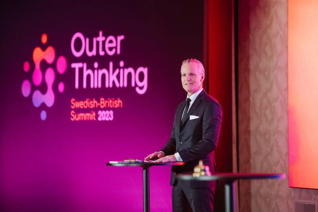 Fredrik Warneryd, VD för Svenska Handelskammaren, talar till publiken och öppnar officiellt toppmötet, klädd i professionell klädsel.