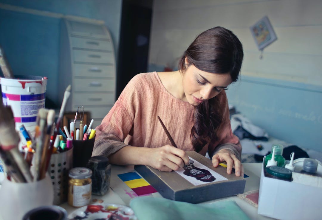Fokuserad kvinna målar på duk bland konsttillbehör i en mysig ateljé.