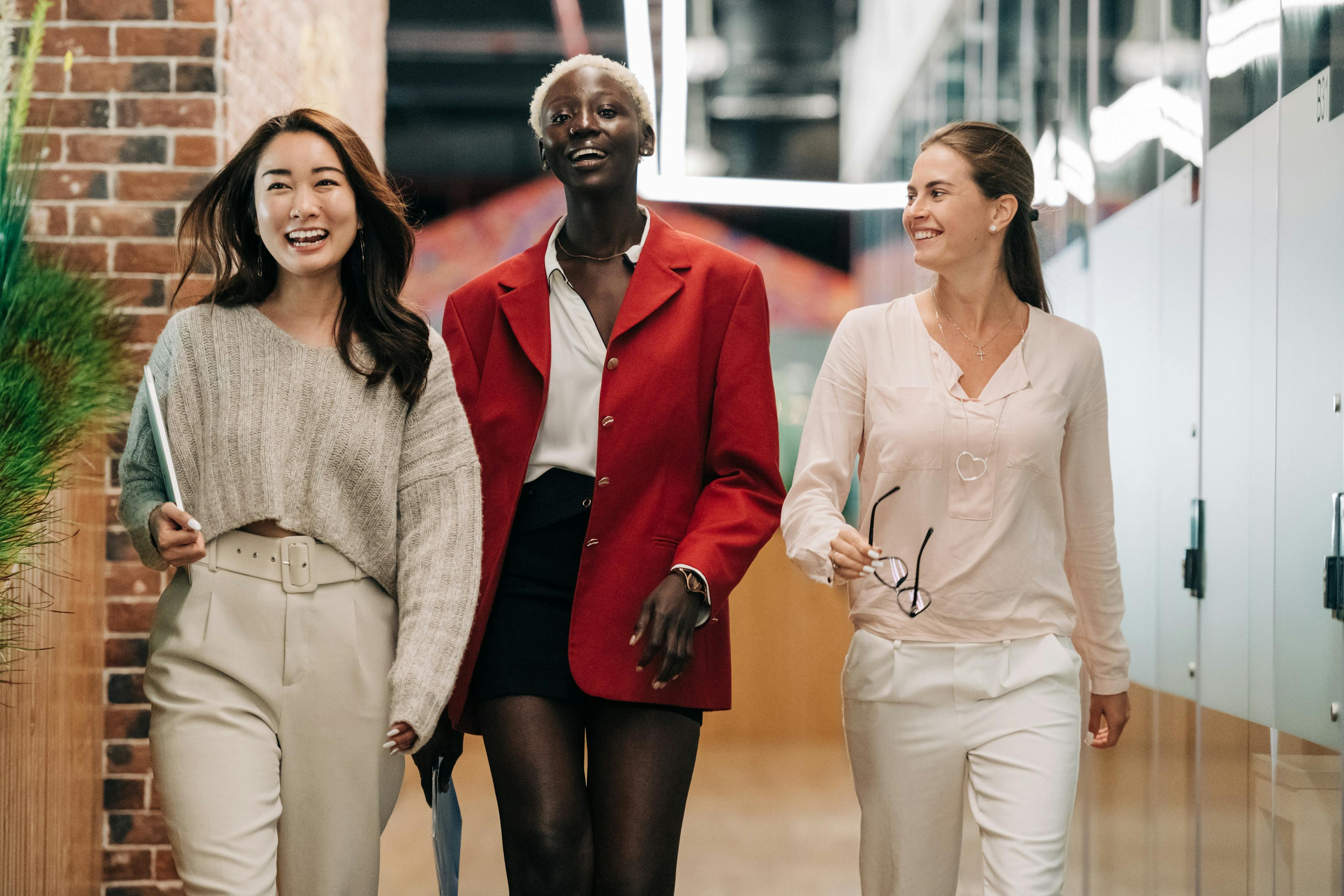 Tre kvinnor på kontoret som skrattar och går tillsammans och främjar en positiv arbetsplatskultur.