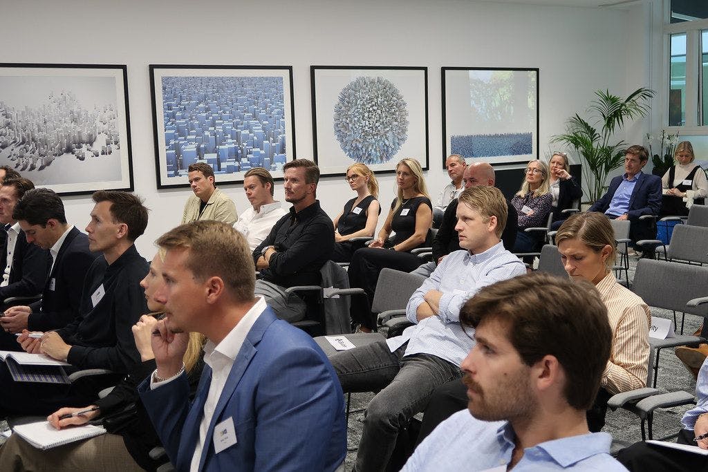 Bild som visar 14 företag som uppmärksamt lyssnar på talare vid ett evenemang.